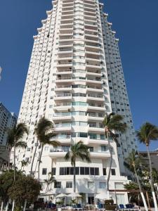a tall white building with palm trees in front of it at Ocean Pacific appartment in Acapulco