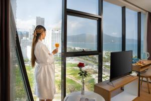 峴港的住宿－KOVA Diamond Hotel Da Nang，窗户前拿着一杯葡萄酒的女人