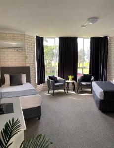 a bedroom with two beds and chairs and windows at Beach Park Motel 