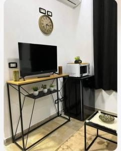 a television on a stand with a clock on a wall at Appartement Cosy aux Jardins de Carthage in Sidi Daoud