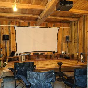 a large white screen in a wooden room with chairs at 　Komori Village GH ～小森ヴィレッジ ゲストハウス～ 自然の中にある庭付平屋一棟貸 