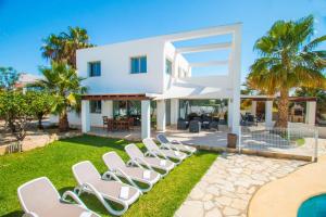 a group of white lounge chairs on a lawn in front of a house at Villa Athos - PlusHolidays in Calpe