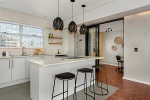 una cocina con armarios blancos y una isla con taburetes. en Doric Court 605, en Ciudad del Cabo