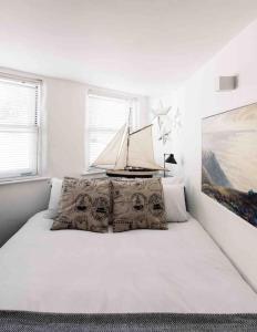 a white bedroom with a bed with pillows and a painting at The Old Stores, Luxury beach side selfcatered holiday cottage above the beach in Porthleven