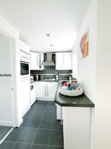 una cucina con armadi bianchi e piano di lavoro nero di White Eden, King bed, Free parking, Private patio, Fast WiFi, Dog, Family, Biker Friendly, Central Cornwall a St Austell