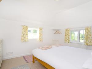 a white bedroom with a bed and two windows at Keepers Cottage in Petersfield