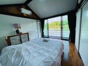 a bedroom with a large bed in a room with windows at เรือนแพคุณมน-Khun Mon Raft in Kanchanaburi