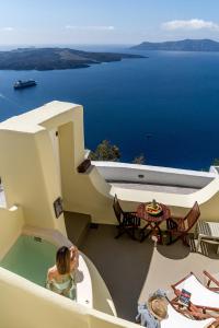 Eine Frau steht in einer Badewanne auf einem Balkon mit Meerblick in der Unterkunft Alma Libre Suites in Fira