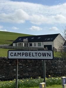 a street sign in front of a stone wall and a house at Inveroran in Campbeltown