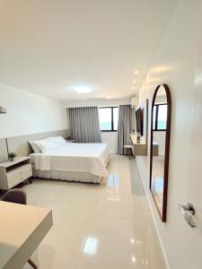 a white bedroom with a bed and a mirror at Praia da Costa, SUNRISE STAY in Vila Velha