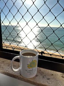 a cup of coffee sitting on a window sill near the ocean at Praia da Costa, SUNRISE STAY in Vila Velha