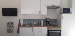 a kitchen with white cabinets and a sink and a refrigerator at Appartement neuf clim terrasse & piscine in Blauzac