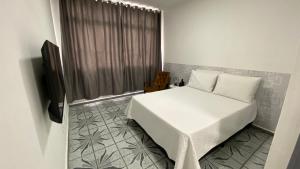 Schlafzimmer mit einem weißen Bett und einem TV in der Unterkunft Apartamento Frente à Praia Santos in Santos