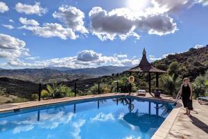 una mujer de pie junto a una piscina con montañas en el fondo en Rural cottage in holiday park with 55 m2 pool en Tolox