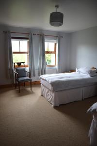 een slaapkamer met een bed en een stoel en 2 ramen bij The White House in Enniskillen
