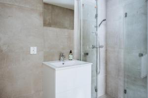 La salle de bains est pourvue d'un lavabo blanc et d'une douche. dans l'établissement Stay Strandgaten - New apartment in city center, à Bergen