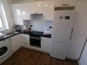 a kitchen with white cabinets and a white refrigerator at White City Apartment, your London stay in London