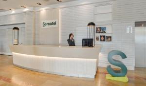 a woman standing at a reception desk in a lobby at Sercotel Kalma Sitges in Sitges