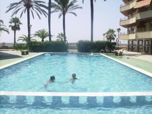two people swimming in a large swimming pool with palm trees at Apartamentos Marina sol de España in Cambrils
