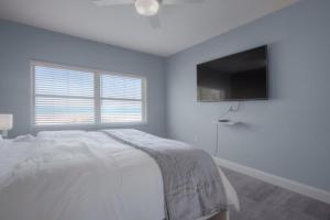 a white bedroom with a bed and a flat screen tv at Shore To Please Beach Oceanfront Patio Pet Friendly in Jacksonville Beach