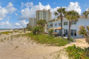 a building on the beach next to a beach with palm trees at Shore To Please Beach Oceanfront Patio Pet Friendly in Jacksonville Beach