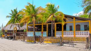 un edificio blanco y amarillo en la playa con palmeras en Hotel Restaurante Spa La Barca de Oro, en Las Peñitas