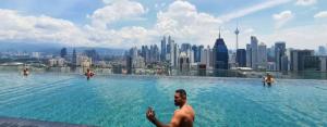 a man sitting in a swimming pool with a city skyline at Regalia Suites KLCC View Rooftop Infinity Pool by Angkasa Homes in Kuala Lumpur