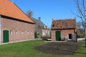 un ancien bâtiment en briques avec une porte verte et une grange dans l'établissement Trekkershuisje 't Zeeuws Knoopje, à Aagtekerke