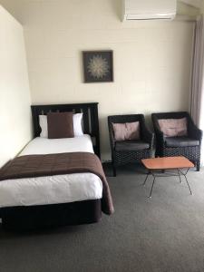 a bedroom with a bed and two chairs and a table at Rosetown Motel in Te Awamutu
