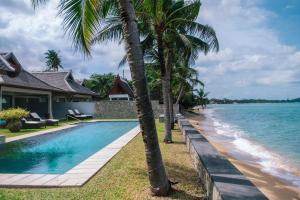 a swimming pool with palm trees next to a house at Miskawaan Villa Wayu in Mae Nam