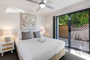 a white bedroom with a bed and a sliding glass door at MARJ12- Stylish and Spacious in Mooloolaba