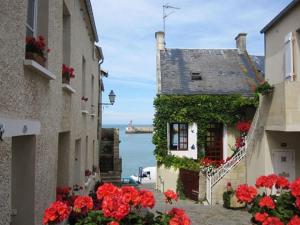a view of the ocean from between two buildings with flowers at La Terrasse du Port - Front de Mer - 10 Personnes in Port-en-Bessin-Huppain