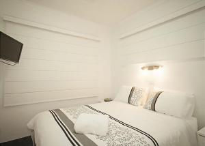 a white bedroom with a bed and a television at Sand Sea 1 in Sawtell