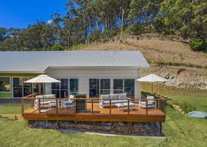 a house with a deck with chairs and umbrellas at Ciao Korora The Mediterranean in Kororo Basin