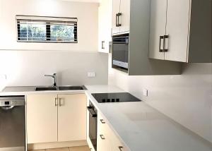 a white kitchen with white cabinets and a sink at Periwinkle in Sawtell