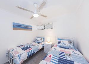two beds in a room with a ceiling fan at Periwinkle in Sawtell