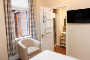 a bedroom with a chair and a window and a television at Alban and Abbey House in Inverness