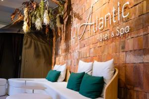 a white couch with green pillows against a brick wall at Atlantic Hôtel & Spa in Les Sables-d'Olonne