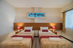 two beds in a hotel room with two lamps at Kuta Suci Guesthouse in Kuta
