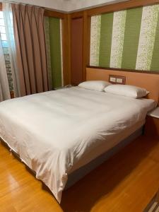 Una cama con sábanas blancas y almohadas en un dormitorio en Mei Hua Hotel, en Kaohsiung