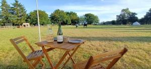 einen Picknicktisch mit einer Flasche Wein und zwei Stühlen in der Unterkunft Le Pressoir de Gisay Camping Car et Caravane Uniquement in Gisay
