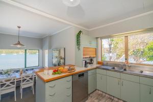 cocina con armarios blancos, mesa y ventanas en Oceans 88 Whitianga Coastal Suites, en Whitianga