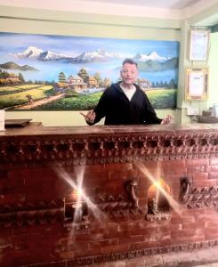 a man standing behind a brick fireplace in front of a painting at Hotel Bhaktapur Inn in Bhaktapur
