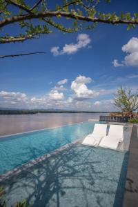uma piscina com duas espreguiçadeiras brancas em frente a um corpo de água em Chewa Khong Nakhon Phanom - SHA Certified em Nakhon Phanom