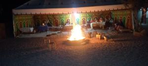 a group of people sitting in a room with a fire at Auberge Restaurant TISSILI " Oasis de Fint" in Fint