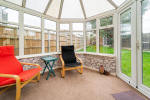 two chairs and a table in a conservatory with windows at Dwellers Delight Living Ltd Serviced Accommodation, Chigwell, London 3 bedroom House, Upto 7 Guests, Free Wifi & Parking in London