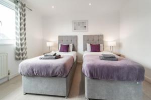 two beds in a bedroom with purple blankets and pillows at Dwellers Delight Living Ltd Serviced Accommodation, Chigwell, London 3 bedroom House, Upto 7 Guests, Free Wifi & Parking in London