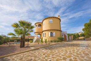 um edifício amarelo com uma palmeira em frente em Villa Ortembach- PlusHolidays em Calpe