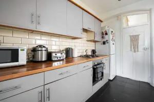 cocina con armarios blancos y encimera de madera en Alross Room with Breakfast, en Londres