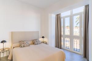 a white bedroom with a bed and a large window at CASA DE LA VEGA SUITES in Chiclana de la Frontera